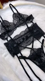 Conjunto de lencería de cuatro piezas en encaje negro, compuesto por bralette, tanga con tiras regulables, portaligas y ligas para piernas.