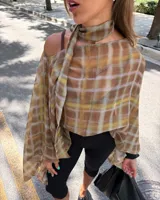 Blusa transparente de gasa con estampado a cuadros en tonos marrón y amarillo, corte asimétrico con hombros caídos y bufanda tipo choker integrada.