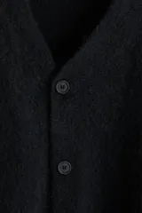 Cárdigan negro de punto peludo suave, con cuello en V pronunciado y cierre frontal de botones. Presenta remates acanalados en puños y bajo.