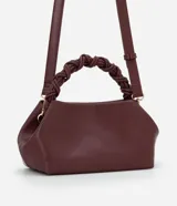 Bolso de mano pequeño color borgoña, con cuerpo de forma trapezoidal y asas cortas trenzadas. El material parece ser cuero sintético (PU).