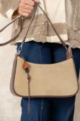 Cartera tipo baguette de diseño minimalista, confeccionada en una combinación de gamuza color beige en el panel frontal y cuero color chocolate en los bordes y la correa. Incluye un detalle colgante de cuentas de madera y cierre superior.