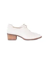 Zapato cerrado tipo mocasín con taco cuadrado de madera, confeccionado en cuero con textura de reptil en color crema. Presenta un detalle de hebilla metálica dorada en el empeine.
