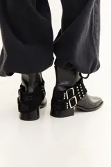 Bota de caña baja confeccionada en cuero con textura crocco, color bordó. Presenta taco cuadrado, punta cuadrada y un accesorio desmontable con doble hebilla metálica y tachas decorativas.