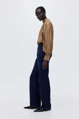 Pantalón de jean de tiro alto con corte recto y pierna ancha. Confeccionado en denim rígido, presenta cierre frontal con botón, bolsillos laterales, bolsillo monedero y bolsillos traseros.