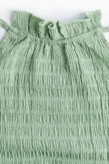 Top corto verde agua con textura arrugada, cuello halter con volantes y lazos para atar en la nuca, espalda descubierta y volantes en el ruedo.