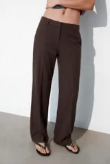 Pantalón de corte recto y tiro bajo, color marrón oscuro. Presenta trabillas en la cintura, bolsillos laterales, falsos bolsillos traseros de vivo y raya planchada en el delantero. Cierre frontal con cremallera, botón interior y ganchos metálicos.