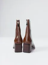 Botas de caña media color marrón, confeccionadas en cuero con acabado brillante. Presentan punta cuadrada, taco de madera y un distintivo bordado decorativo en color rojo que recorre el empeine hasta la punta.