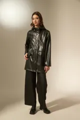 Pilot de efecto cuero negro con acabado brillante, diseño de manga larga, capucha con cordones ajustables y cierre frontal con botones a presión. Cuenta con bolsillos laterales con solapa.