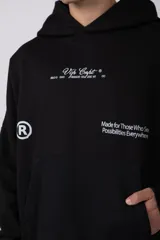 Buzo canguro negro con capucha, confeccionado en algodón frizado de alto gramaje. Presenta estampado gráfico en el pecho con tipografía cursiva y texto, además de un logo circular en la manga. Cuenta con bolsillo frontal tipo canguro, puños y ruedo acanalados.