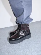 Bota corta de cuero negro tipo biker, con suela track de goma, plataforma, costuras y bordados decorativos en hilo rojo. Presenta tiras con hebillas metálicas y cierre en la parte trasera.