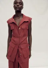 Chaleco largo de estilo utilitario color rojizo, con cuello solapa, sin mangas y cierre frontal con botones. Presenta cuatro bolsillos de parche con solapa en la parte delantera y un acabado con efecto arrugado.