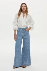 Camisa blanca de algodón con cuello alto, detalles de encaje broderie en el frente, mangas abullonadas y puños con volados y encaje. Cierre frontal con botones tapados.