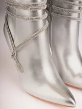 Botines plateados con terminación en punta y taco aguja. Decorados con tiras de strass que se enrollan alrededor del tobillo y se atan en el empeine.