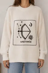 Sweater de punto negro con diseño oversize, cuello redondo y manga larga. Presenta un bordado frontal en color crudo con motivo del signo del zodíaco Géminis, acompañado de detalles de sol, luna y estrellas dentro de un recuadro.