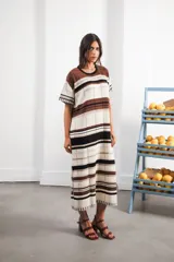 Vestido largo de tejido calado con rayas horizontales en tonos beige, marrón y amarillo. Tiene corte recto, hombros caídos, tajo lateral y logo bordado en la manga.