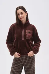 Buzo de polar tipo peluche color chocolate, con cuello alto y cierre frontal parcial. Presenta un bolsillo frontal con cierre y detalle de tela técnica en contraste.