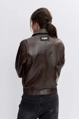 Cazadora de efecto piel en color marrón chocolate, con cuello clásico, cierre frontal con cremallera, bolsillos laterales y puños con botón.