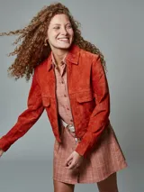 Campera corta tipo cazadora color naranja, de gamuza, con cuello clásico, cierre frontal y bolsillos con solapa en el pecho.