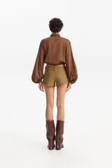 Camisa de manga larga abullonada, color marrón con estampado animal print sutil, cuello camisero y cierre frontal de botones. La parte inferior se anuda al frente dejando ver parte del abdomen.