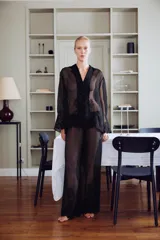 Blusa semitransparente negra de cuello solapa y manga larga, con cierre frontal de botones y detalles de bordados tonales en el ruedo y los puños.
