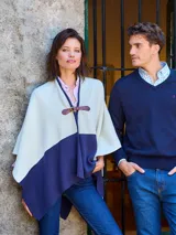 Ruana de tejido de punto con diseño bicolor en tonos crudo y azul marino, con cierre frontal mediante hebilla de cuero ajustable.
