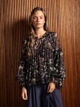Blusa de gasa con estampado abstracto en tonos oscuros, cuello redondo con lazo ajustable, corte holgado con frunces y mangas largas abullonadas con puños elásticos.