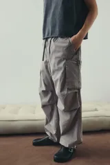 Pantalón cargo de algodón color gris claro, con corte holgado y cintura elástica ajustable con cordón. Presenta bolsillos cargo grandes en las piernas, pliegues cosidos en las rodillas y cordones ajustables en los bajos.