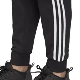 Pantalón de jogging Adidas modelo Essentials, color negro con las icónicas tres bandas blancas laterales. Presenta cintura elástica con cordón ajustable, corte cónico y puños acanalados en los tobillos.