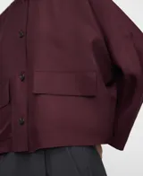 Camisa corta bordó de línea recta, con escote redondo a la base, manga japonesa y cierre frontal con botones. Cuenta con bolsillos delanteros de plastrón con solapa.