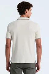 Polo de manga corta confeccionada en tejido piqué con textura tipo waffle, color beige. Presenta cuello clásico con cierre de botones y detalles de líneas en contraste en el borde del cuello y las mangas. Incluye el logo de la marca bordado en el pecho.