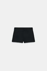 Shorts de tiro medio color negro, con bolsillos delanteros y falsos bolsillos con solapa en la parte trasera. Cierre frontal con cremallera y ganchos metálicos.