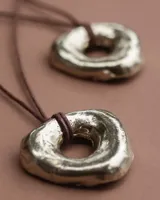 Collar artesanal con dije circular de diseño orgánico e irregular, realizado en bronce y alpaca maciza, suspendido de un hilo de algodón natural.