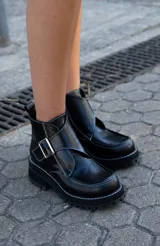 Botas cortas de cuero negro con hebilla plateada, costuras blancas contrastantes y suela track.