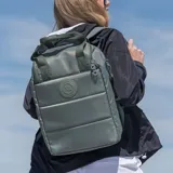 Bolso matero verde de poliéster con diseño acolchado. Tiene acceso con cierre doble, múltiples bolsillos internos y externos, compartimentos para notebook y matero, asas fijas, correa regulable y herrajes plateados.