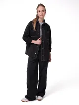 Camisa de denim color negro con costuras en contraste, corte oversized, cuello camisero, cierre frontal con botones metálicos y bolsillos dobles en el pecho.