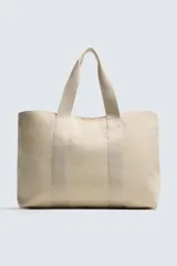 Bolso tipo shopper de tejido de algodón color beige claro, con dos asas de mano y cierre magnético en el compartimento principal. Incluye un bolsillo interior con cierre de cremallera.