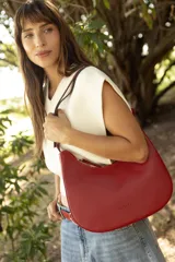 Cartera hobo de cuero color rojo con silueta curva de media luna, cierre superior y correa de hombro ajustable.