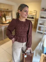 Blusa color chocolate con diseño de frunces elásticos en el frente y la espalda, mangas largas abullonadas con puños elásticos y corte peplum.