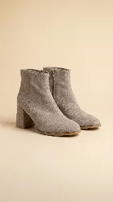 Botas de caña alta desmontables de gamuza color beige, con taco cuadrado de 6 cm y punta semi cuadrada. Presentan un diseño con costura central y detalle de estribo con hebilla forrada en el tobillo.