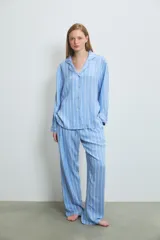 Pijama de dos piezas confeccionado en viscosa, compuesto por una camisa de manga larga con cuello solapa y cierre frontal de botones, y un pantalón de corte recto y holgado. Presenta un diseño de rayas verticales en tonos azul y blanco.