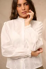 Camisa blanca de manga larga con detalles bordados en vertical, cuello mao con volados y cierre frontal con botones.