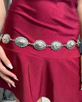Cinturón de cadena estilo western compuesto por eslabones circulares de metal plateado con diseño grabado y una pequeña piedra central clara en cada pieza.