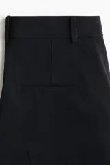 Pantalón ancho negro de corte holgado con pinzas, cierre frontal oculto y pliegues marcados en las piernas.