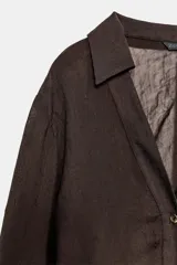 Camisa marrón oscuro de manga larga con cuello solapa y escote pico. Presenta un tejido con textura sutilmente arrugada y drapeados fruncidos en los laterales frontales. Cierre frontal con botones dorados.