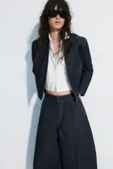 Cazadora bomber de denim color azul oscuro, con escote en pico, cierre frontal cruzado con botones a presión y bajo elástico en los laterales. Cuenta con mangas largas y bolsillos de vivo.