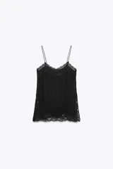 Top lencero de escote en pico con tirantes finos, confeccionado en tejido fluido con aplicaciones de encaje a tono en el escote, laterales y bajo. Presenta aberturas laterales en el ruedo.