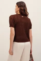 Cardigan de punto metalizado color marrón, de manga corta y diseño abierto al frente con cierre de botón único y detalle de flor aplicada.