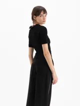 Top Charlotte de algodón y lino color negro, con calce al cuerpo, largo a la primera cadera, frunces en el exterior y escote semi alto con volado, al igual que los puños de las mangas cortas.
