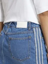 Falda mini de denim azul con diseño clásico de cinco bolsillos y cierre frontal con botones. Presenta las icónicas tres tiras de la marca en los laterales.