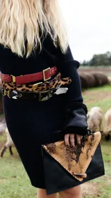 Sobre de cuero color rojo y negro con diseño de vaca y cierre con botón de guampa.